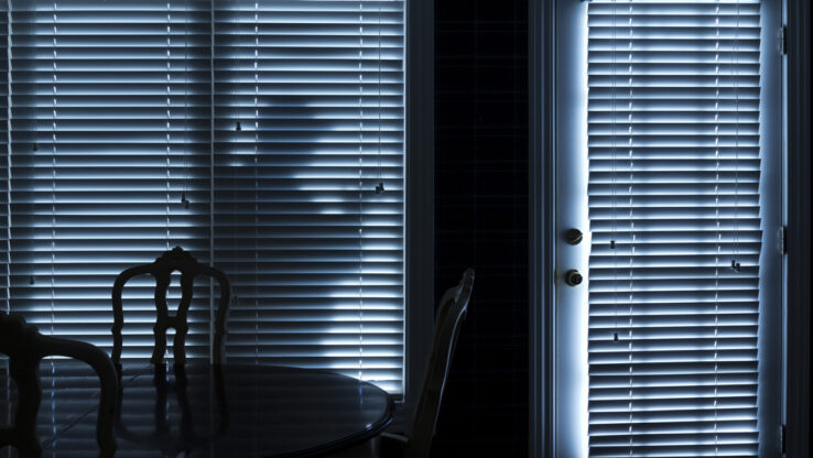 Silhouette eines Einbrechers, der nachts zur Hintertür schleicht