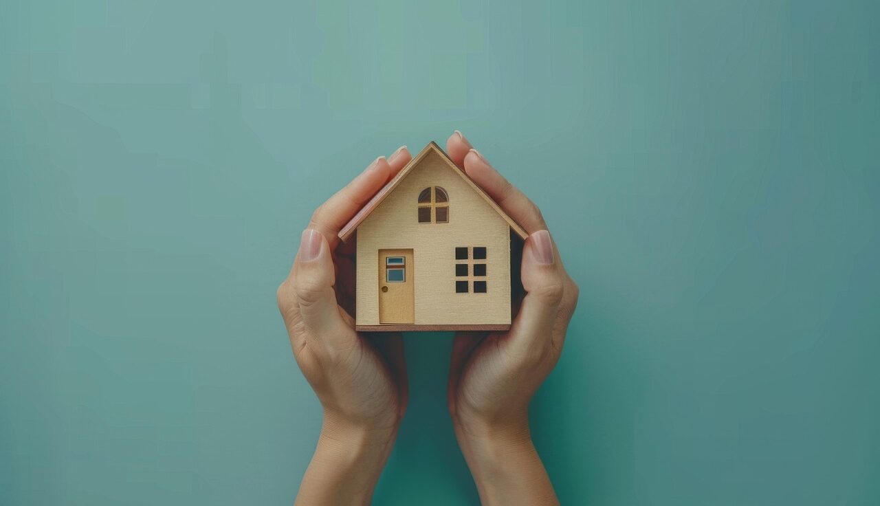 Zwei Hände die ein Modellhaus halten.