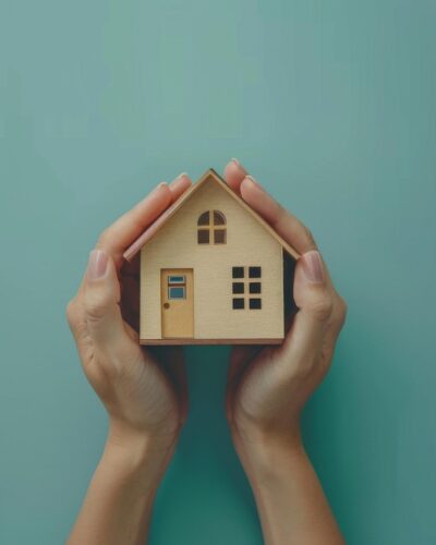 Zwei Hände die ein Modellhaus halten.